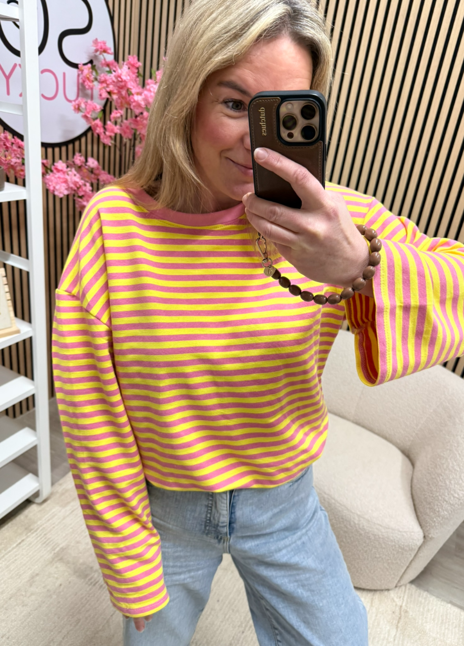 model draagt gestreepte longsleeve Maud geel donkerroze oversized langer model op een jeans – So Lucky