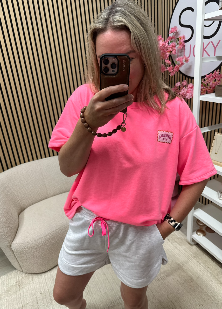 Model draagt Sweater T-shirt California Club neon roze met zomerse outfit – So Lucky